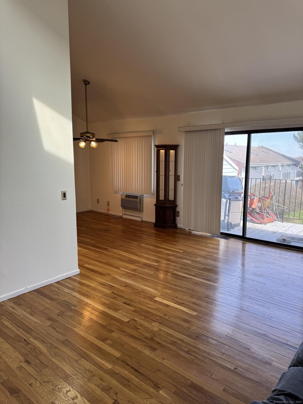 unfurnished living room featuring a wall unit AC, baseboards, ceiling fan, and wood finished floors
