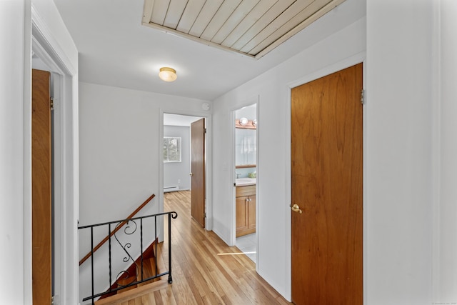 corridor with light wood-type flooring, a baseboard radiator, a sink, and an upstairs landing