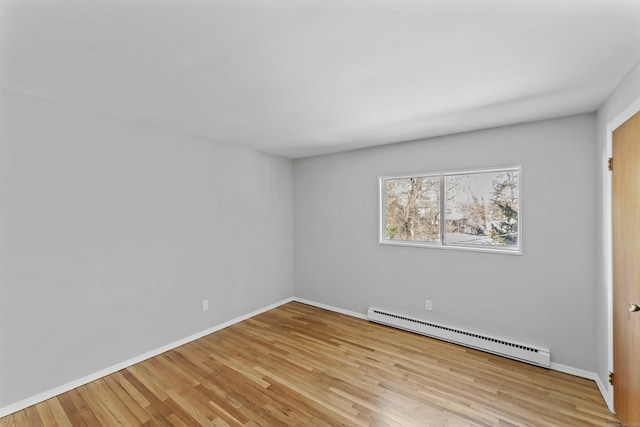 unfurnished room featuring a baseboard heating unit, baseboards, and light wood-style floors