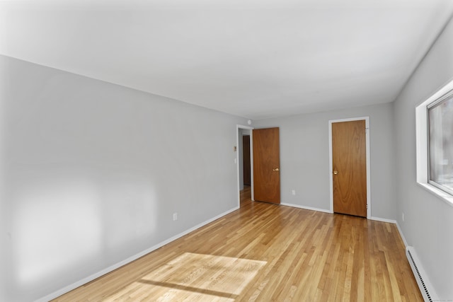 unfurnished bedroom with light wood-type flooring, baseboards, and baseboard heating