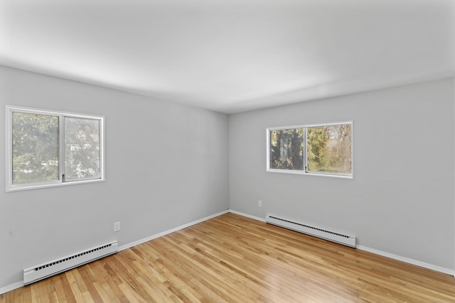 unfurnished room featuring a baseboard heating unit, light wood-type flooring, baseboards, and baseboard heating