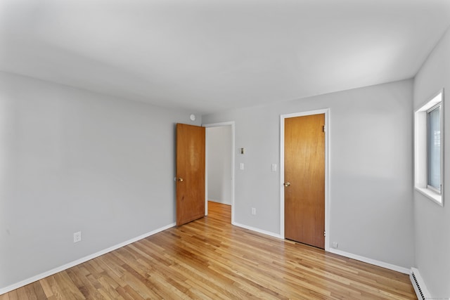 unfurnished bedroom featuring a baseboard heating unit, baseboards, and light wood-style floors