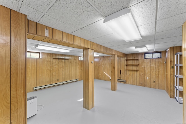 basement featuring a drop ceiling, wood walls, and baseboard heating