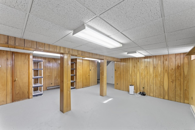 finished below grade area featuring a paneled ceiling, wood walls, and a baseboard heating unit