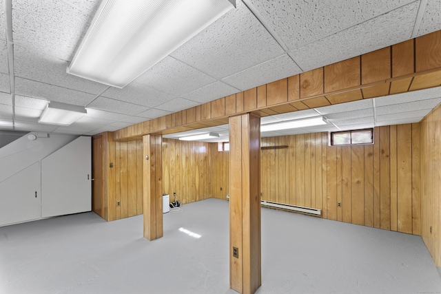 basement with a baseboard heating unit, a paneled ceiling, and wooden walls