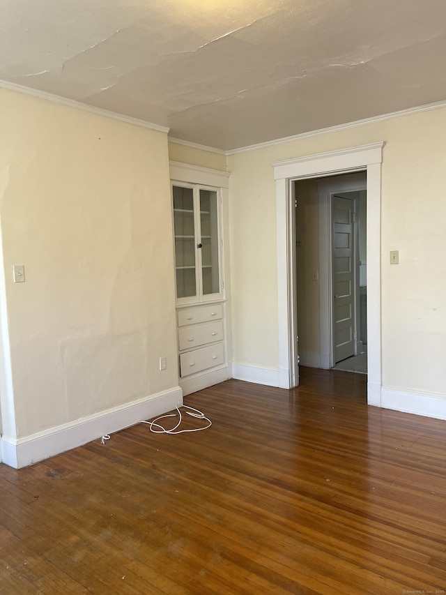 spare room with ornamental molding, dark wood-style flooring, and baseboards