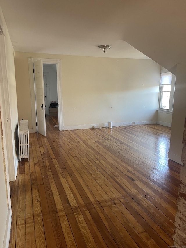 spare room featuring baseboards, wood finished floors, and radiator