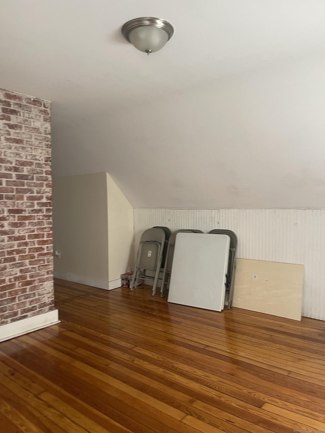 additional living space with vaulted ceiling, dark wood finished floors, and brick wall