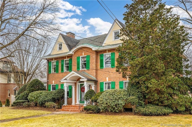 view of front of property with brick siding, a chimney, and a front yard