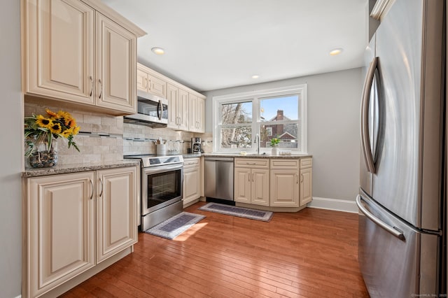 kitchen featuring appliances with stainless steel finishes, a sink, decorative backsplash, and light stone countertops