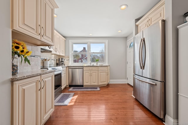 kitchen featuring light wood-style flooring, appliances with stainless steel finishes, light stone counters, cream cabinets, and backsplash