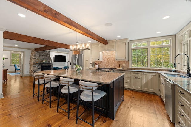 kitchen featuring open floor plan, a kitchen island with sink, stainless steel appliances, pendant lighting, and a sink