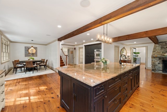 kitchen featuring a spacious island, beamed ceiling, a stone fireplace, pendant lighting, and a sink