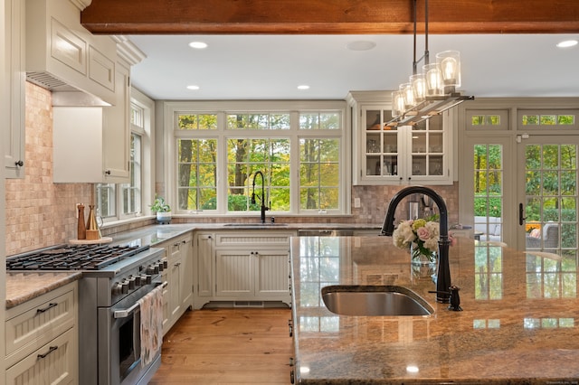 kitchen with dark stone countertops, glass insert cabinets, a sink, and stainless steel stove