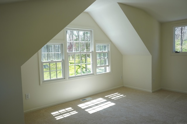 additional living space featuring baseboards, visible vents, vaulted ceiling, and light colored carpet