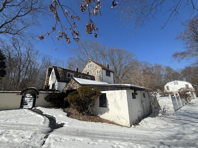 view of snowy exterior with stone siding, a fenced front yard, and a gate