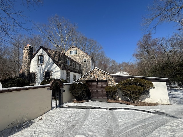 view of front facade with stone siding, a fenced front yard, a chimney, an attached garage, and a gate