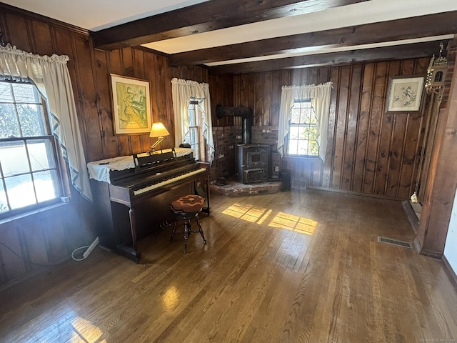 sitting room featuring wood walls, wood finished floors, visible vents, beam ceiling, and a wood stove