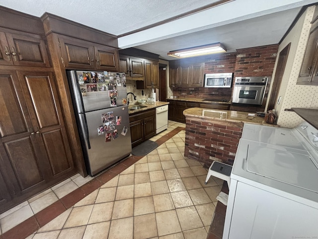 kitchen with washer and clothes dryer, stainless steel appliances, a textured ceiling, a sink, and light tile patterned flooring