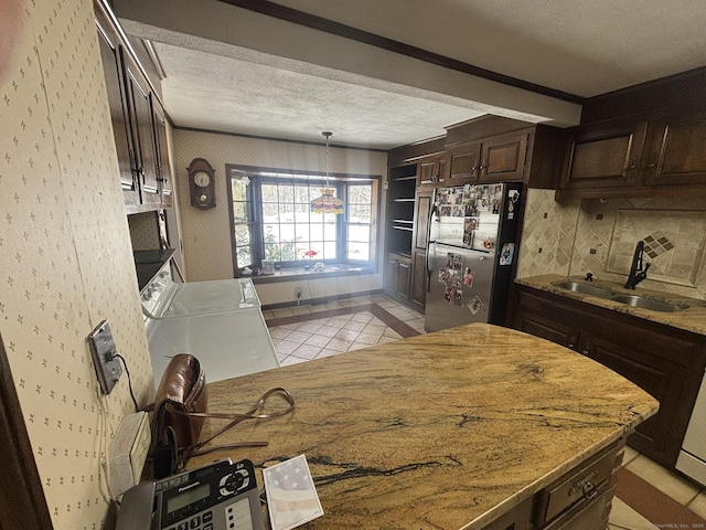 kitchen featuring a textured ceiling, a sink, dark brown cabinets, freestanding refrigerator, and washer / dryer