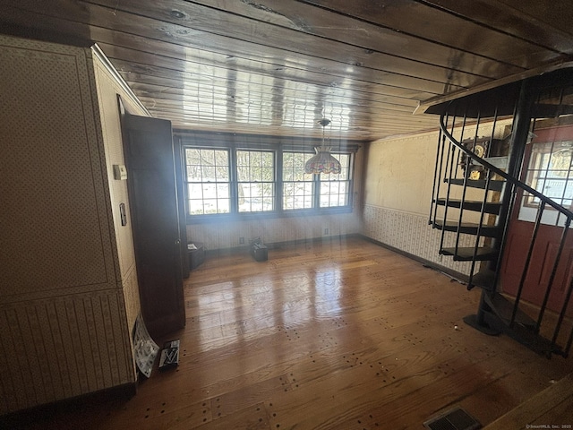 unfurnished living room featuring wallpapered walls, visible vents, wainscoting, hardwood / wood-style floors, and stairs