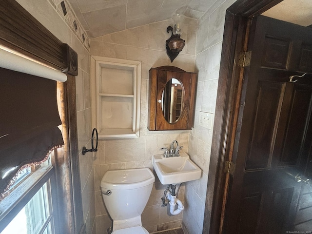 bathroom featuring toilet, a sink, vaulted ceiling, and tile walls