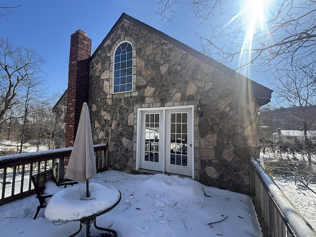 snow covered house featuring stone siding and a chimney