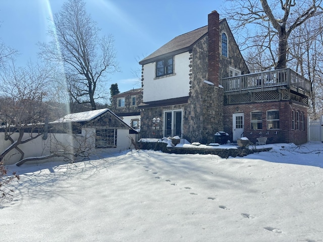 snow covered house with stone siding, a chimney, and an outbuilding