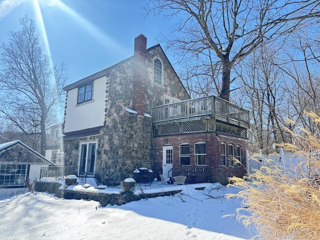 snow covered back of property with brick siding, a chimney, and a balcony