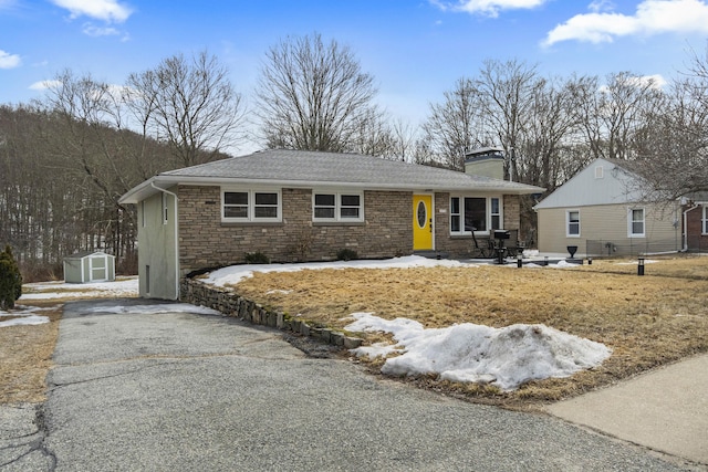 single story home with driveway, a storage shed, stone siding, a chimney, and an outbuilding