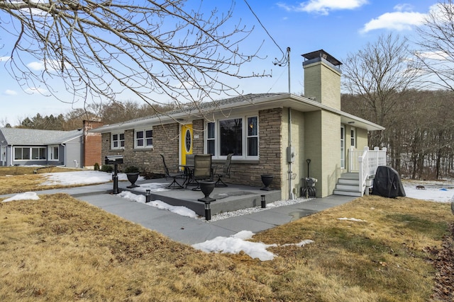 ranch-style house with a patio area, stone siding, brick siding, and a chimney