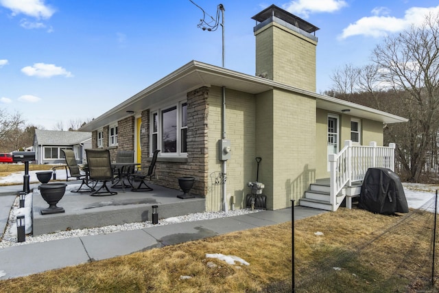 view of side of home featuring brick siding, a patio, and a chimney