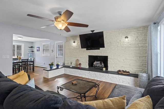 living room featuring a baseboard heating unit, brick wall, a fireplace, wood finished floors, and baseboards