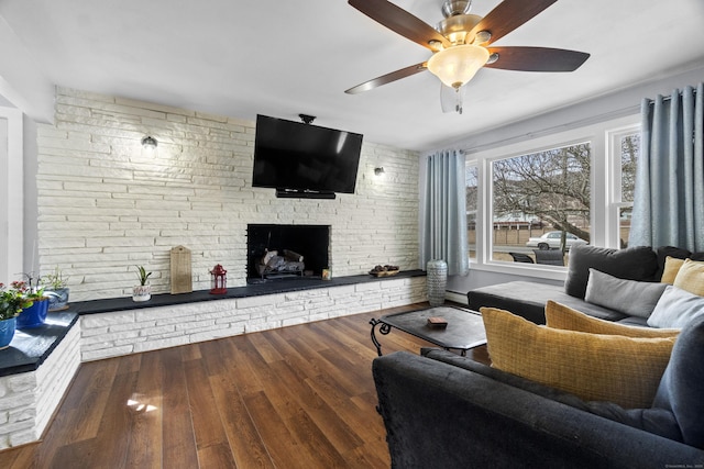 living room with brick wall, a fireplace, a ceiling fan, and wood finished floors