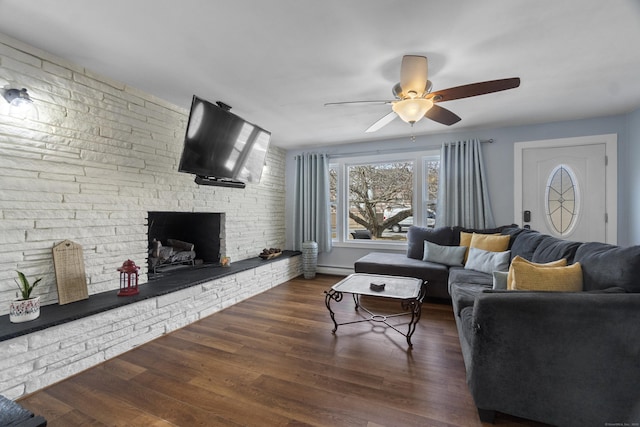 living room featuring a large fireplace, brick wall, a ceiling fan, baseboard heating, and dark wood finished floors