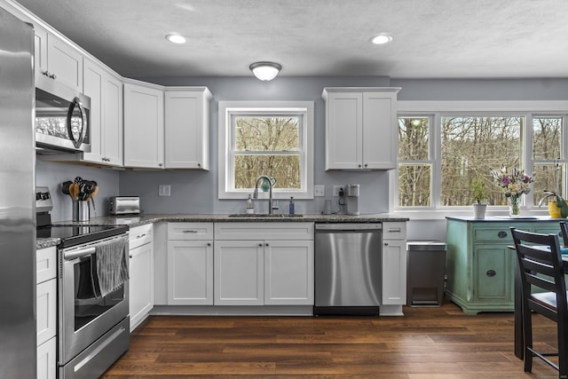 kitchen featuring stainless steel appliances, dark stone countertops, a sink, and white cabinets