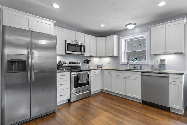 kitchen featuring stainless steel appliances, stone countertops, white cabinetry, and a sink