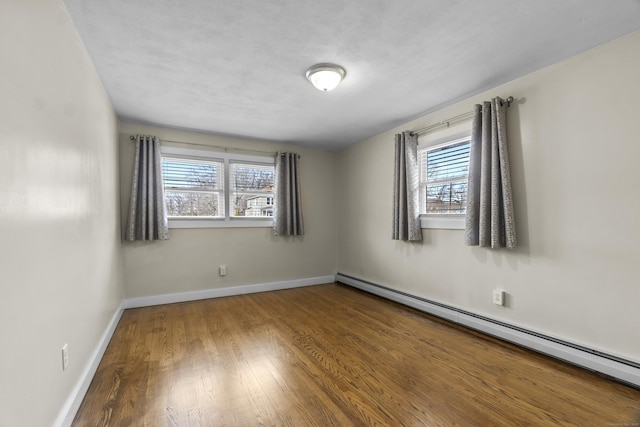 unfurnished room featuring a baseboard radiator, baseboards, and wood finished floors