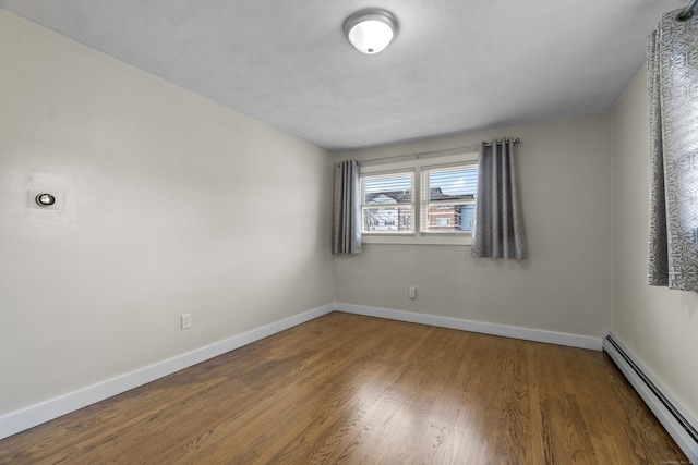 empty room featuring a baseboard radiator, wood finished floors, and baseboards