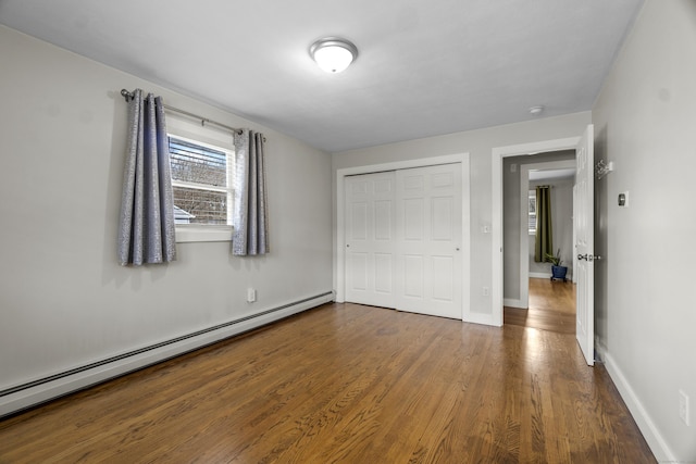 unfurnished bedroom with baseboards, a baseboard heating unit, a closet, and wood finished floors