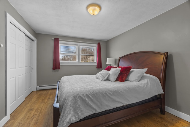 bedroom with a closet, a baseboard radiator, wood finished floors, and baseboards