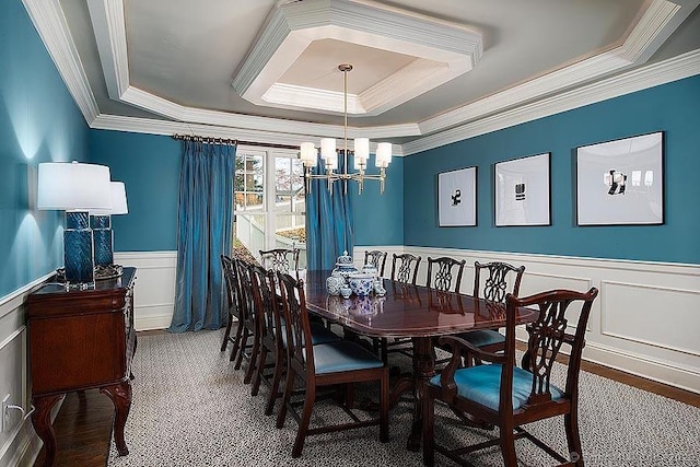 dining area with a chandelier, a wainscoted wall, a raised ceiling, and crown molding