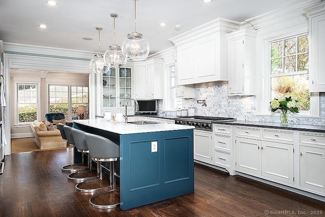 kitchen with pendant lighting, a sink, a center island with sink, glass insert cabinets, and stainless steel gas stovetop