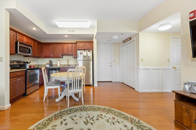 kitchen featuring wainscoting, stainless steel appliances, light wood-type flooring, a sink, and recessed lighting