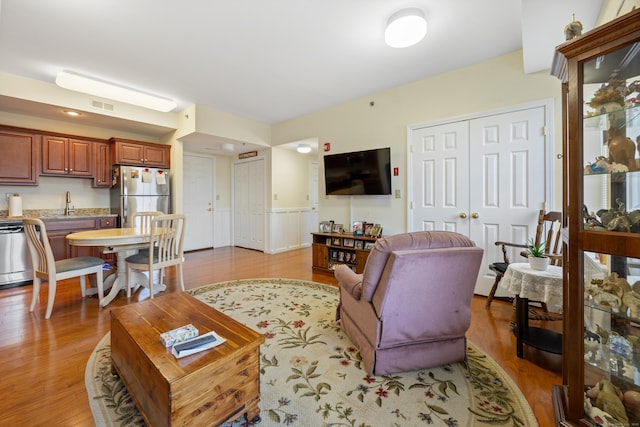 living area featuring light wood-style floors, visible vents, and wainscoting