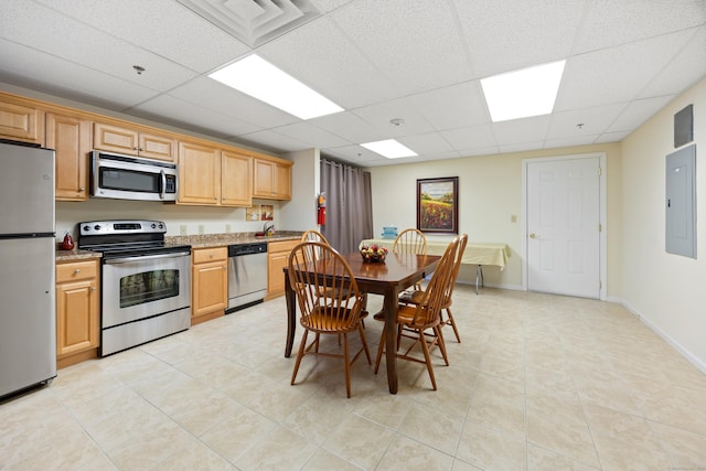 kitchen featuring a drop ceiling, appliances with stainless steel finishes, a sink, light stone countertops, and electric panel