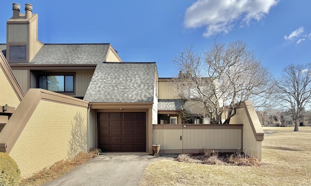 exterior space featuring an attached garage, driveway, a chimney, and roof with shingles