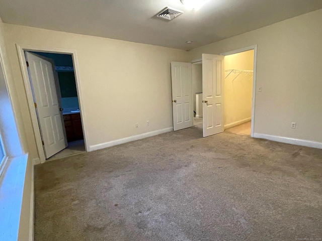 unfurnished bedroom featuring visible vents, a spacious closet, carpet flooring, connected bathroom, and baseboards