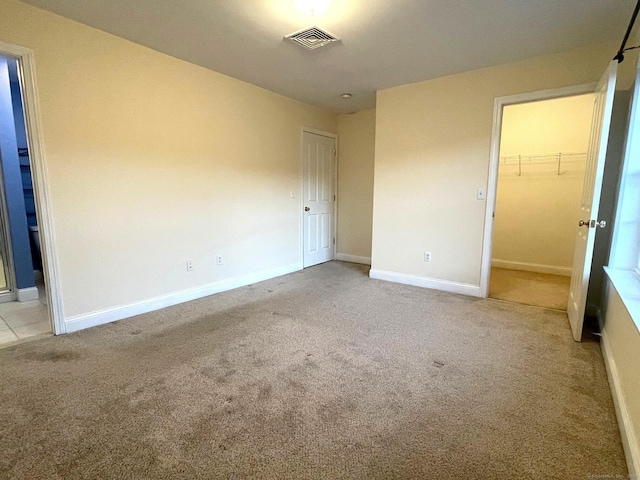 unfurnished bedroom featuring baseboards, visible vents, a walk in closet, carpet flooring, and a closet