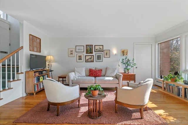 living room with a baseboard heating unit, light wood-type flooring, crown molding, and stairs